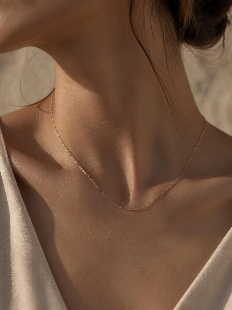 Cadena fina de oro sobre el cuello, fondo neutro desaturado