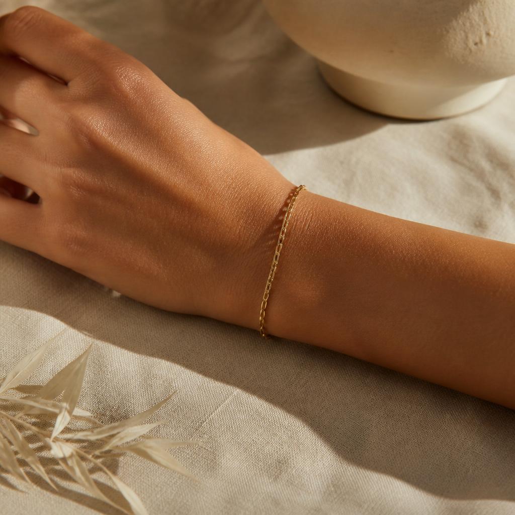 Muñeca con pulsera delgada de oro sobre mesa de lino